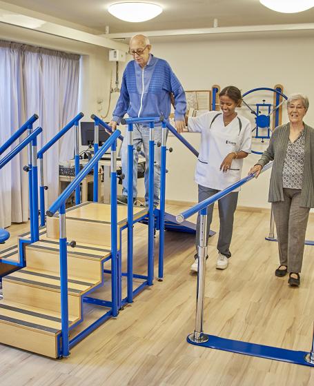 Dos personas mayores en la sala de fisioterapia haciendo ejercicios con la supervisión de la fisioterapeuta